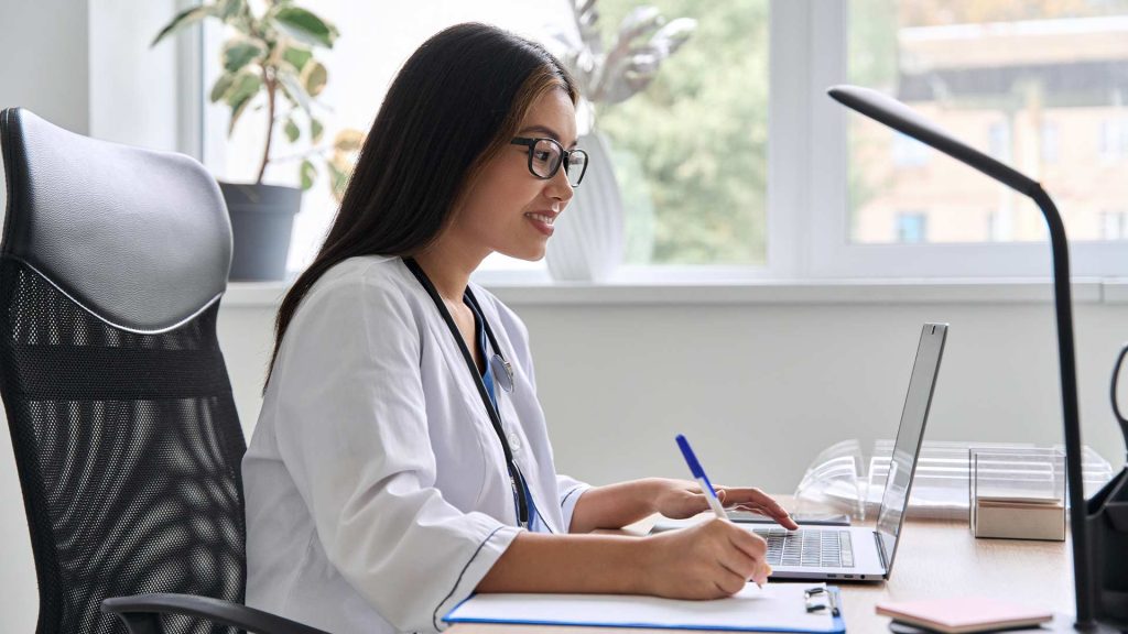 Back Office Virtual Assistant - A focused woman in a medical uniform works diligently at her computer, suggesting her role in providing behind-the-scenes administrative support.