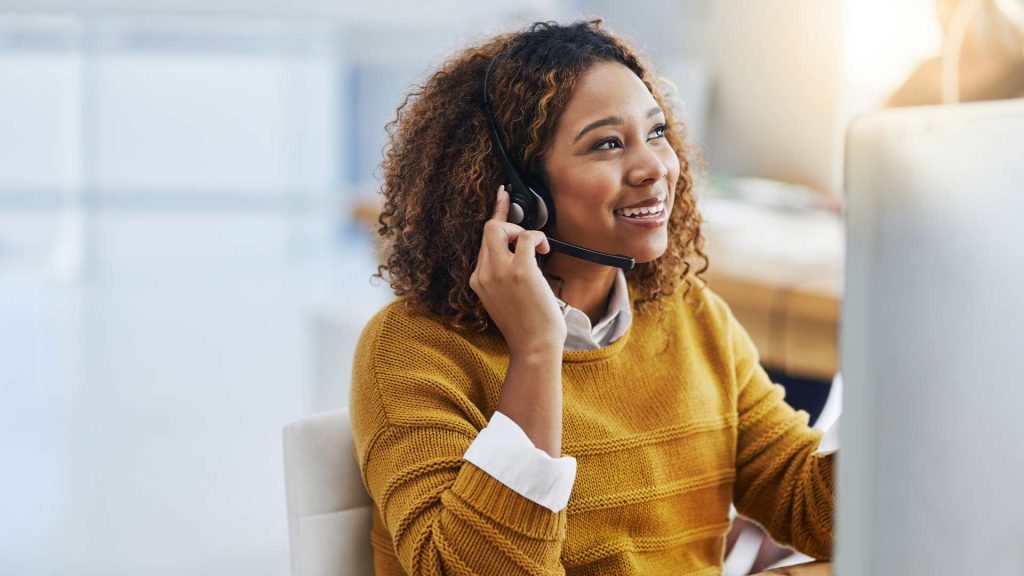 hire social media assistant: A smiling woman with a headset, suggesting to be a social media assistant assisting customers or clients.