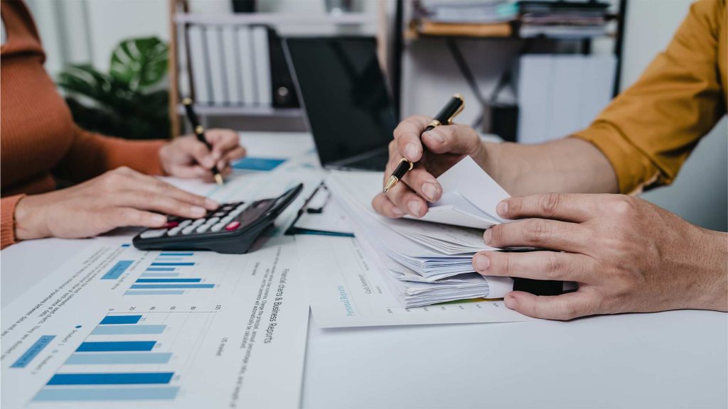 Hands of a person working on financial documents and using a calculator, representing the concept of virtual assistant bookkeeping.