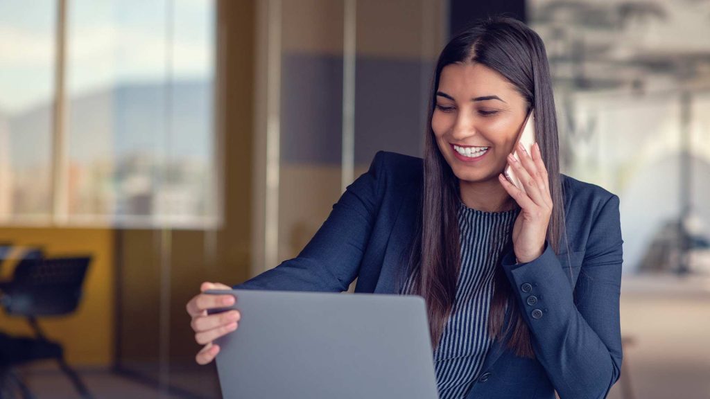 A smiling woman in business attire using a laptop computer, working as a virtual accounting assistant to provide remote financial services or support.